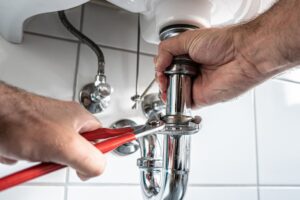 Close-up of a plumber using a wrench to tighten or repair a chrome drainpipe under a bathroom sink, illustrating the importance of professional plumbing maintenance in Castle Rock, CO.