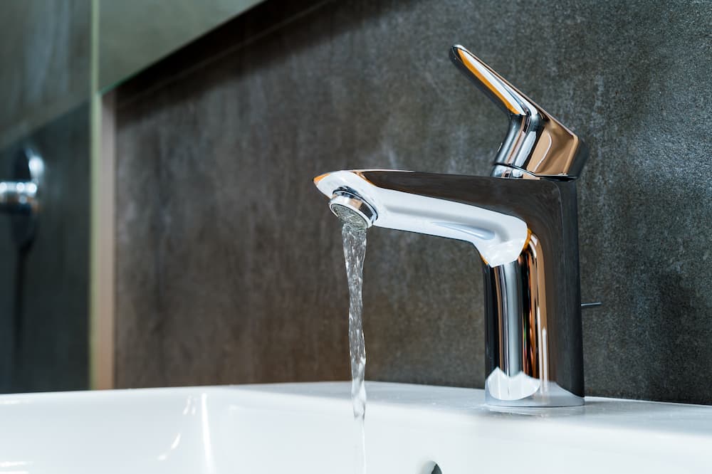 Chrome bathroom faucet with running water over a white sink, highlighting the importance of inspecting water flow and drains for potential issues requiring sewer line maintenance in Highlands Ranch.