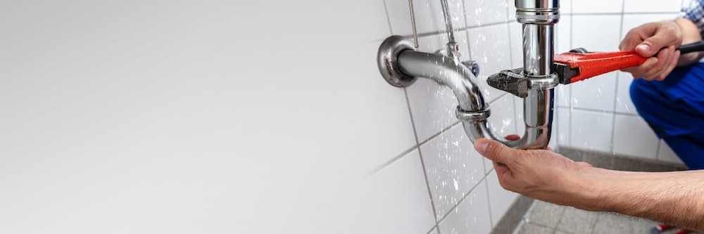 Professional local plumber fixing a visible leak on bathroom drain plumbing, used to advertise sewer line repair in Parker, CO.